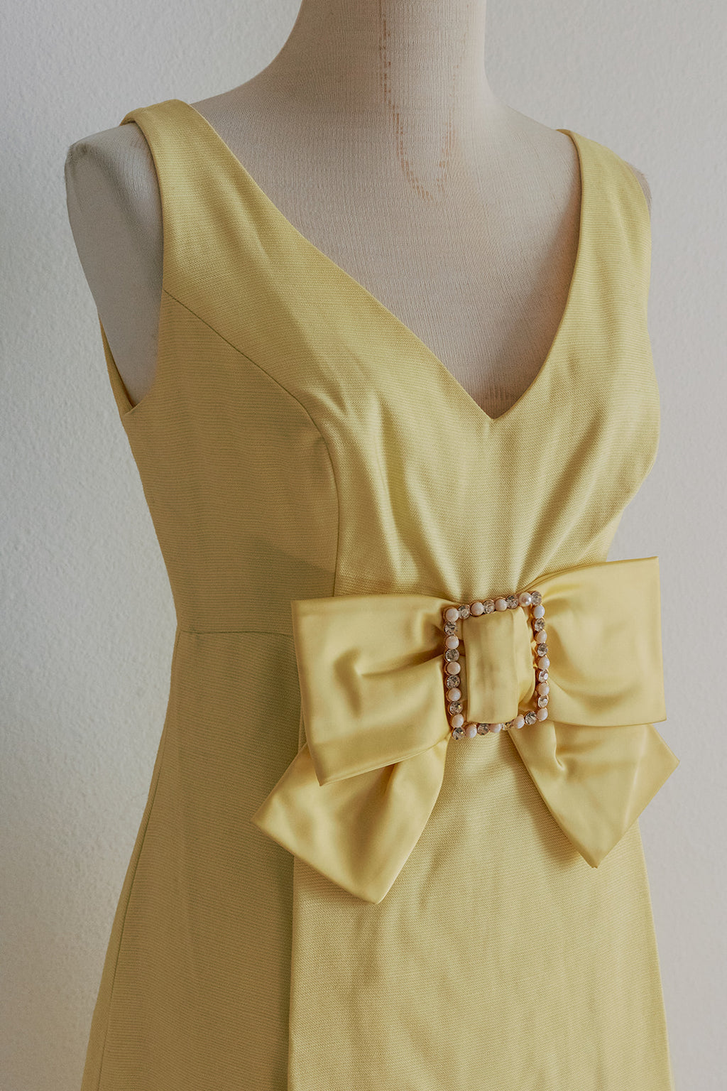 Yellow dress with a large bow on a mannequin against a plain background